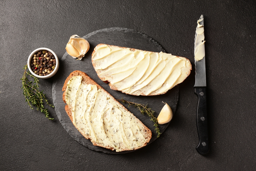 Sneden brood besmeerd met huisgemaakte look- en kruidenboter op een leisteen plank, met look en tijm